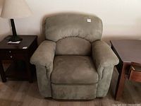 Front view of single upholstered recliner chair beside side table and lamp.