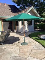 Green Majestic Market patio umbrella fully opened on stone patio with metal base and wooden pole