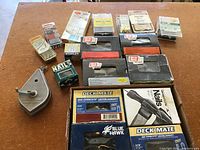 Photo of assorted packaged nails, screws, fasteners, and staples on a table showing multiple labeled boxes and blister packs of various sizes and brands.