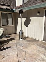 Full view of the freestanding propane patio heater positioned on a stone patio against a beige exterior wall.