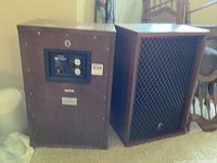Side by side view of two wooden cabinet Sansui speakers, one showing back panel with control dials and inputs, the other showing black mesh grille front.
