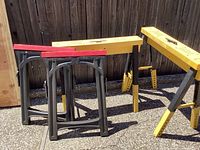 Two yellow PACK HORSE folding sawhorses alongside two black plastic folding sawhorses with red tops.