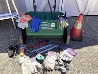 Full view of Scotts AccuGreen 3000 seeder with work gloves on top and other tools, caster wheels, and traffic cone in foreground.