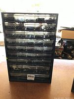 Front view of a large black plastic small parts organizer with multiple clear drawers, some drawers contain screws and hardware, product tag visible.