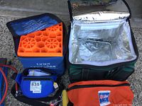 Green insulated cooler bag open revealing silver lining next to blue medical bag and orange first aid bag with orange foam insert visible inside one cooler.