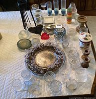 Mixed variety of candle holders on a white quilted surface including metal, glass, ceramic, and wooden types