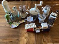 Wide shot of all kitchen items on wooden table including appliances, bottles, molds, and tools.
