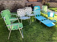 Side view of six aluminum outdoor chairs with woven straps, and one blue aluminum lounge chair on green grass