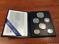 Open black coin presentation case showing six Canadian coins in clear capsules and certificate inside.