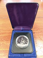Blue velvet-lined display case open with the 1975 Canadian silver dollar coin in a plastic capsule centered inside.