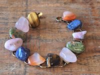 Photo of gemstone bracelet arranged in a circle showing multiple polished stones including tiger's eye, rose quartz, sodalite, carnelian, and unakite connected by metal links.