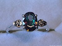 Close-up of sterling silver ring with oval mystic topaz gemstone showing intricate side detail and reflective surface.