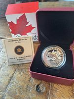 Photo of coin in open red presentation box with certificate and outer cardboard box showing maple leaf and year 2013.