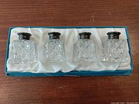Four crystal base salt and pepper shakers with sterling silver tops, presented in a blue box with satin lining.