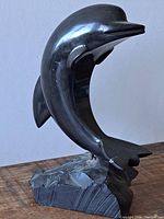 Side view of the black stone dolphin sculpture on rough stone base.