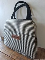 Front view of the J. Greensports thermal lunch bag showing black and white stripes, black handles, and brand patch.