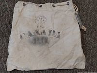 Overall view of the white canvas mail bag with faded Canada P.O. black stencil and crown emblem, showing metal grommets and drawstring at the top.