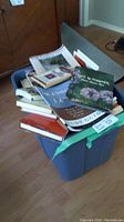 A large blue bin filled with a variety of hard and soft cover books, some with visible titles related to self-help and personal development.