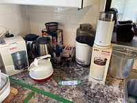 Overview of all coffee and popcorn making appliances on a kitchen counter, showing boxed Salton coffeemaker, kettles, grinders, popcorn poppers, and scale, miscellaneous items clustered together.