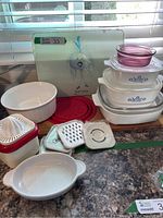 Photo showing Tina Turnip ceramic cutting board, white round French casserole, red juicer, graters and slicer plates, red silicone prep trays, and white ceramic dish with handles.