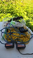 Lot contents including yellow 14-gauge 3-way extension cord, two Ohey Li-ion 21V batteries, and other cords and splitters in a clear plastic bin on a white table outdoors.