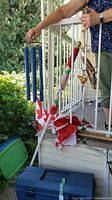 Flags and various wind chimes grouped together on a porch, showing blue tube wind chime, Canadian flags, and a red and white wind chime with gold ball top.