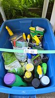 Blue plastic tub containing multiple garden care items such as spray bottles, seed packets, and fertilizer bags, displayed from above.