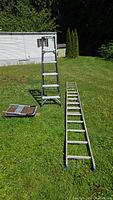 View of all items: fiberglass step ladder, aluminum extension ladder, and hand cart placed on grass.