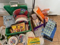 Green plastic bin filled with various party supplies including plates, napkins, cups, cutlery, cake decorations