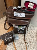 Photo showing the vintage Petri camera in a brown leather half-case with strap, two extra lenses, a black leather Petri case, lens cap, and brown camera bag.