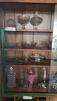 Full shelf display showing a wider variety of glass items including vases, bowls, oil lamp, and serving plates