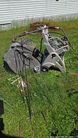 Beige plastic hose reel containing coiled gray garden hose, multiple watering wands, and several black metal plant supports on grassy yard