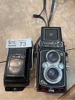 Front view of Yashica Mat 124 camera alongside its black leather carrying case displaying Yashica logo.