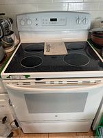 Front view of the white GE electric stove showing a radiant heat glass top with four cooking zones and control knobs. The stove has a digital control panel above the oven door.