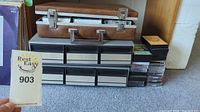 Photo showing the brown leather cassette case on top of three gray plastic cassette tape storage drawers with cassette tapes.