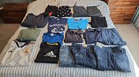 Full layout of assortment clothes on bed showing jeans and shirts