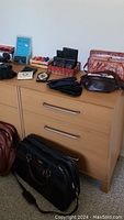 Photo showing assortment of wallets, gloves, and small boxes arranged on wooden dresser including a pair of black gloves, decorative jewelry-like boxes, and a dark brown pointed pouch.