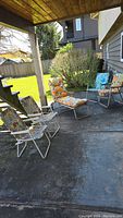Four vintage outdoor lounge chairs on concrete patio, floral cushions, white metal frames, two with wooden armrests