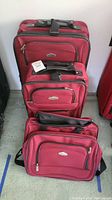 Set of three red fabric suitcases stacked vertically showing brand logo and multiple zippered compartments