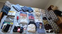 Full layout view of clothing items arranged on a bed, including shirts, socks, pants, and packaged undershirts.
