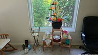 Photo showing assortment of planters, vases and wooden plant stand arranged near a window.