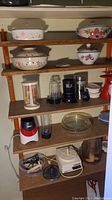Multiple shelves showing ceramic baking dishes with floral patterns, blender, toaster, small kitchen items.