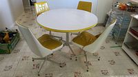 Wide view of retro round table with four yellow and white chairs in room, showing set layout and condition.