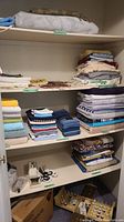 Photo of shelving with folded blankets on the top shelf, towels and linens on middle shelves, and sewing machines on bottom rack.
