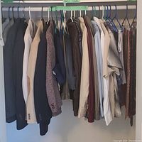 Hanging rack of assorted men's clothing including multiple suit jackets, dress shirts, and pants in various styles and colors.
