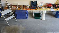 Overview of entire lot showing two wooden benches with assorted tools on top, metal step ladder on left, electrical wire, tool cases, and bins underneath.