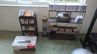 Overall view: two CD stands filled with CDs, Toshiba DVD/VCR box on floor, metal shelf with stereo boombox and extra CDs