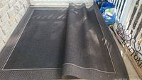 Photo of large black area rug partially rolled, showing overall size and general appearance.