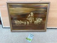 Photo showing framed artwork of a dog sled team with a person guiding eight dogs, mounted in a simple muted frame on a wood floor.