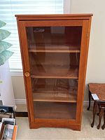 Wood cabinet with glass door front view showing shelves inside.